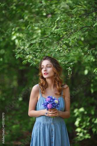 beautiful girl in a denim sundress walks with a bouquet of hyacinths in the garden, spring mood