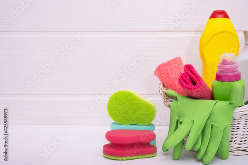 wicker basket with colored household cleaning liquids, colored brushes and rags