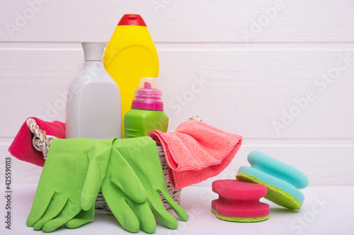 colored bottles with liquid for cleaning the house, colored rags and brushes, green gloves in a basket