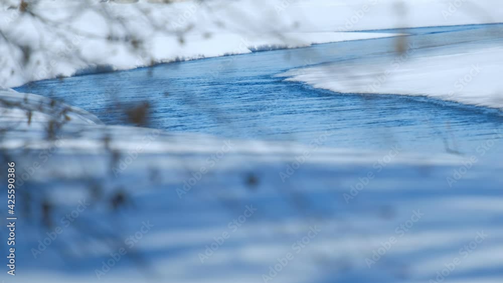 View of the river flow between the snow-covered banks through the branches of trees