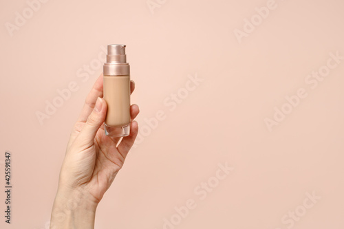 Hand holding makeup liquid found, Applying foundation for makeup. Woman's hands with neutral manicure holding bottle of concealer or toner foundation, copy space, banner, flyer