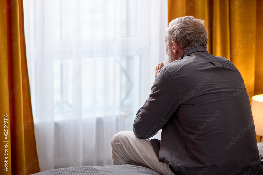 rear view on depressed senior man sitting on bed at home