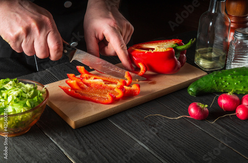 Close-up of chef hands cutting peppers on cutting board. Professional preparation of salad in the kitchen in a restaurant or cafe
