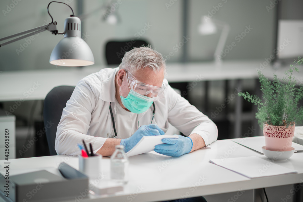 An elderly doctor at the clinic fills out patient records after an appointment in his office at the desk An elderly doctor at the clinic fills out patient records after an appointment in his office at the desk