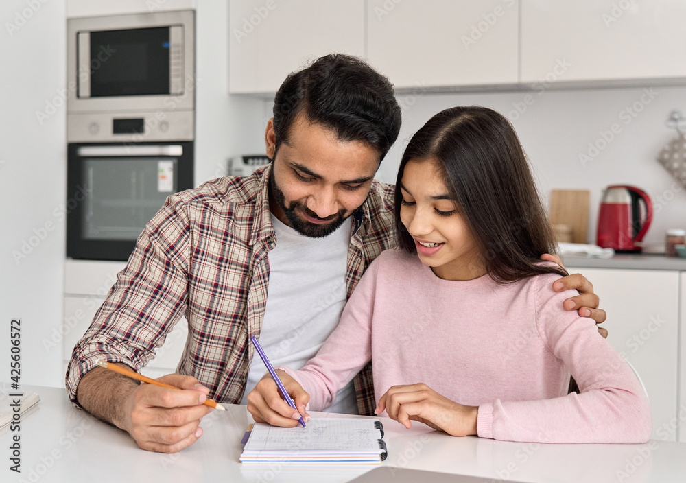 Happy indian father helping school child embracing teen daughter studying at home. Young dad explaining kid teenage daughter learning in kitchen together, doing homework. Parenthood and homeschooling. Happy indian father helping school child embracing teen daughter studying at home. Young dad explaining kid teenage daughter learning in kitchen together, doing homework. Parenthood and homeschooling.