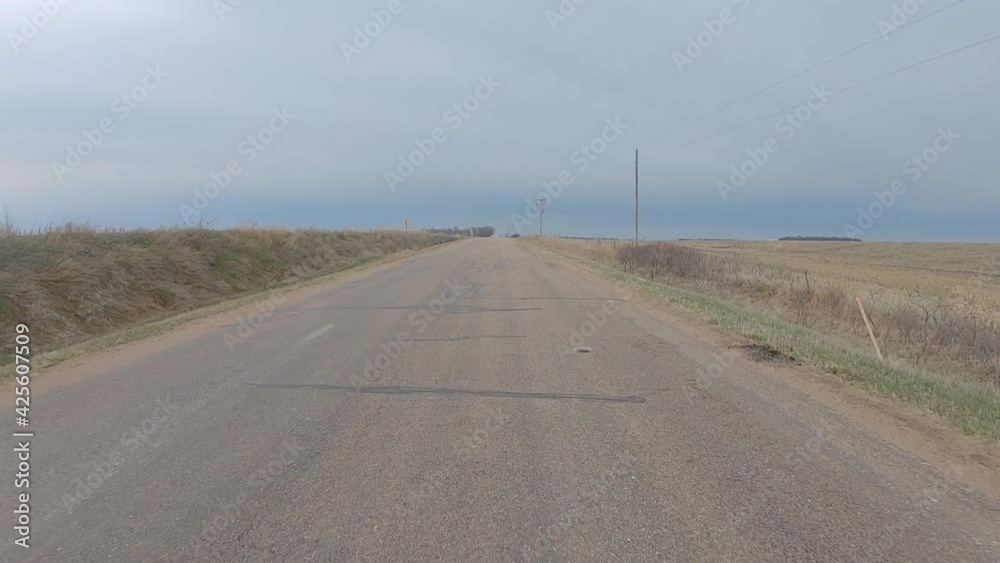 Rear window view while driving on an old asphalt road between harvested fields in rural south central Nebraska on a cloudy winter day; lonely road; point of view Rear window view while driving on an old asphalt road between harvested fields in rural south central Nebraska on a cloudy winter day; lonely road; point of view