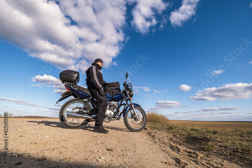  man in a black uniform on bike against the backdrop of panorama of field and blue sky. motorcycle travel concept