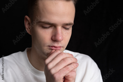young guy folded his hands in prayer, portrait on black background