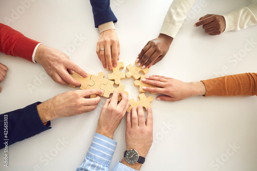 Multiracial business team assembling puzzle. Multiethnic people putting together jigsaw pieces on white table, view from above, high angle shot. Modern enterprise, teamwork, project strategy concept photo