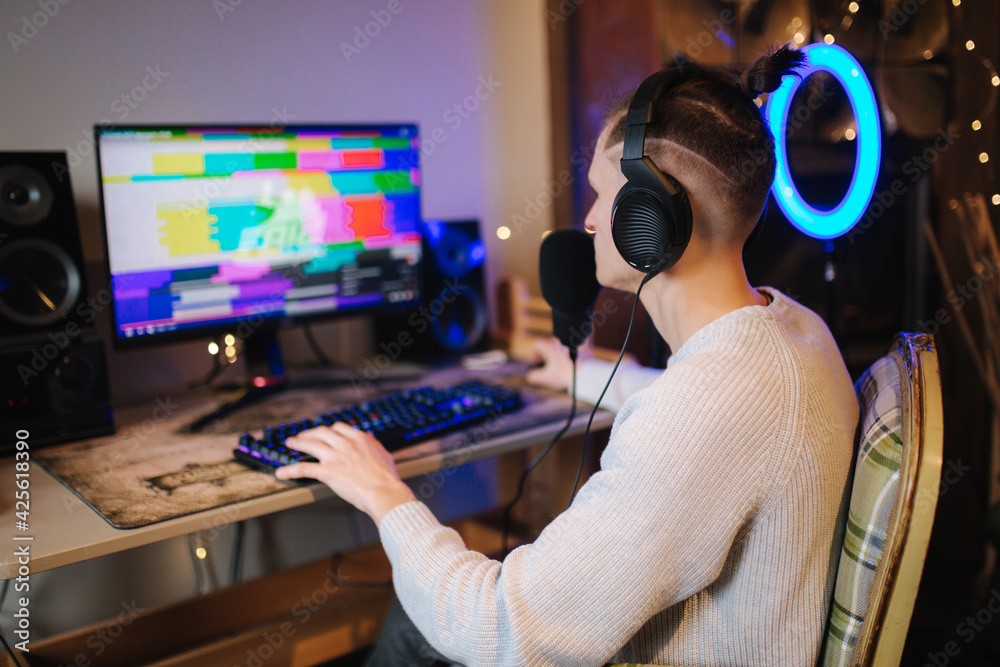 Men playing online video games at home using powerful computer. Streamer man using professional microphone, keypad, mouse in gaming home studio. Back view