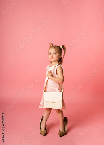 a little girl in a lace dress and shoes with a purse on a pink background with a place for text
