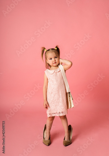 a little girl in a lace dress and shoes on a pink background with a place for text