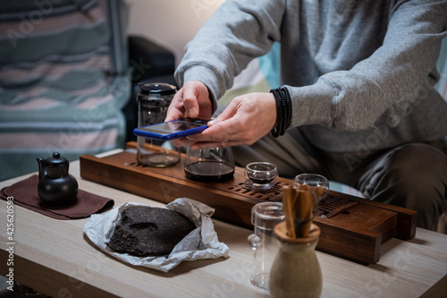 The master of tea harmonies teaches his subscribers in social networks the correct location of the tools of the tea set on the tray. Takes photos on his smartphone.