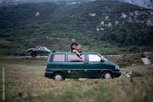 Young man sitting on the roof of his green camper van © Miguel Serrano
