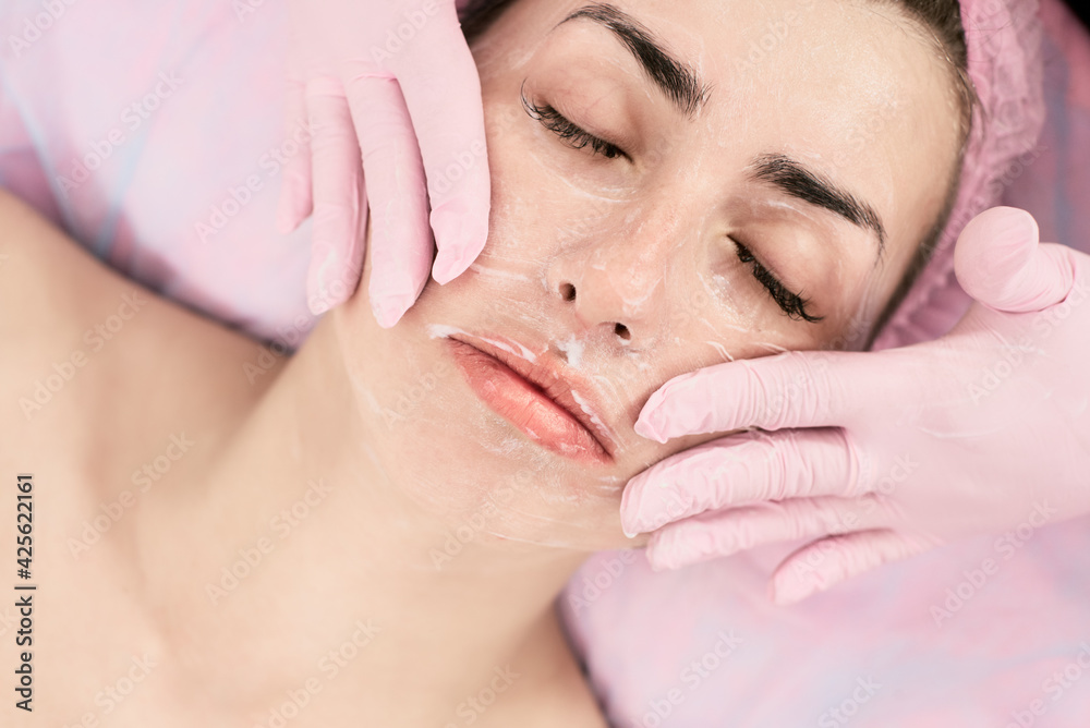 Cosmetologist applaying anti-aging cream on female face in beauty salon, caring for the face and body