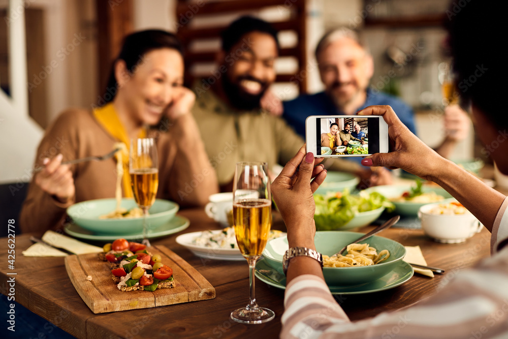 Close-up of black woman photographing her friends during lunch at dining table.