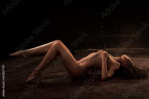 Beautiful nude woman chained on floor looks away