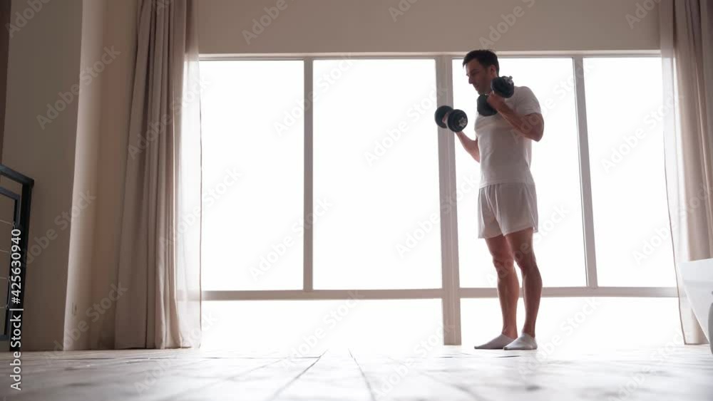 Keep training. Full length view of active caucasian man wearing home clothes exercising with dumbbells at home Keep training. Full length view of active caucasian man wearing home clothes exercising with dumbbells at home