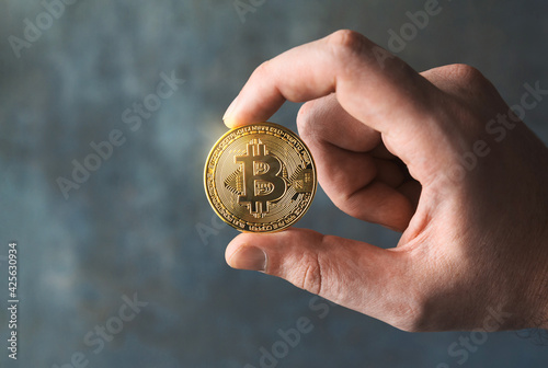 Close up shot of a man's hand showing a golden bitcoin. BTC and cryptocurrencies business on a digital decentralized finances concept