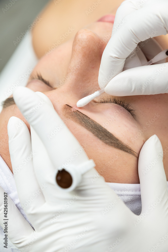 Zbliżenie na proces makijażu permanentnego. Kobieta w salonie urody w trakcie zabiegu pigmentacji brwi.  - obrazy, fototapety, plakaty 