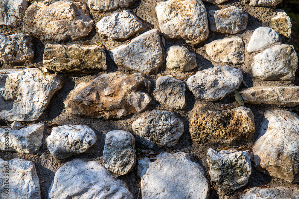 A portion of wall made of rough stones. The side sunlight highlights the volumes and shapes.Stones texture to be used as a background.