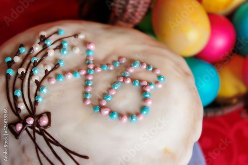 Homemade kulich (cake): a traditional Russian treat for Easter on blurred background of painted colorful eggs. Festive pastries with the letters "XB" on the icing. Close up sweet confectionery decor.