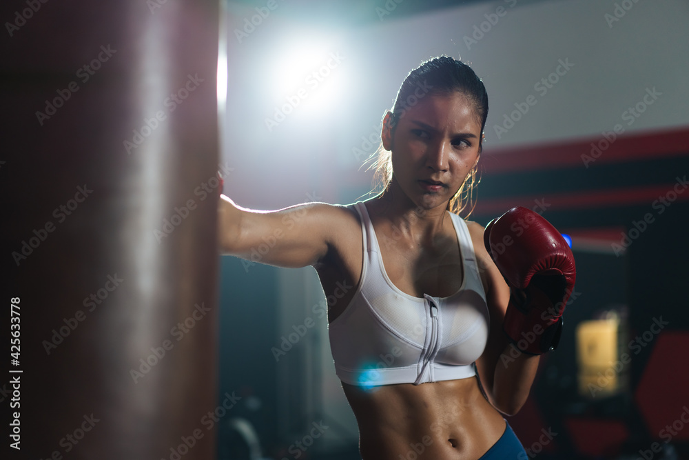 Young Asian doing boxing or Muay Thai punching sandbag in fitness club or gym. healthcare and sport concept.