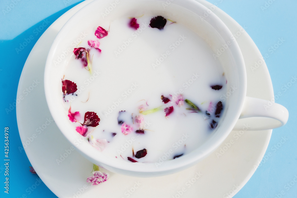White Cup with vegan milk and flowers on a blue background. Concept of vegetarian drinks and food, herbal teas, beauty and health, Spa White Cup with vegan milk and flowers on a blue background. Concept of vegetarian drinks and food, herbal teas, beauty and health, Spa