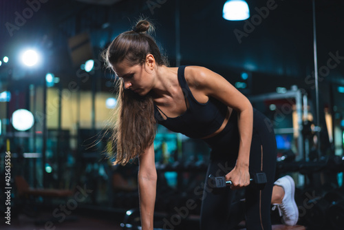 Caucasian young woman in sportswear lifting dumbbell in fitness club or gym.
