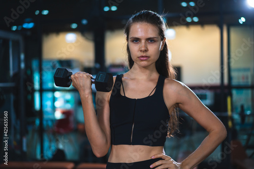 Caucasian young woman in sportswear lifting dumbbell in fitness club or gym.