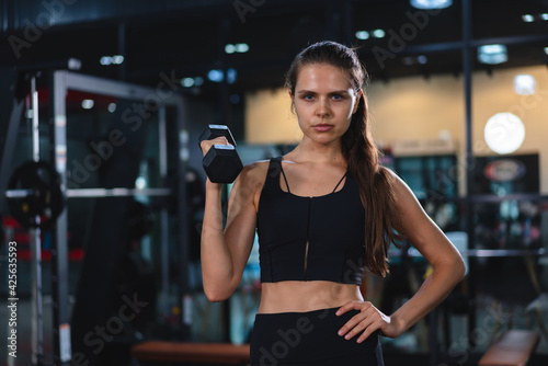 Caucasian young woman in sportswear lifting dumbbell  in fitness club or gym.