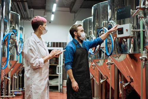 Wallpaper Mural Young female brewery expert and male worker in protective masks testing new beer production equipment during working process Torontodigital.ca