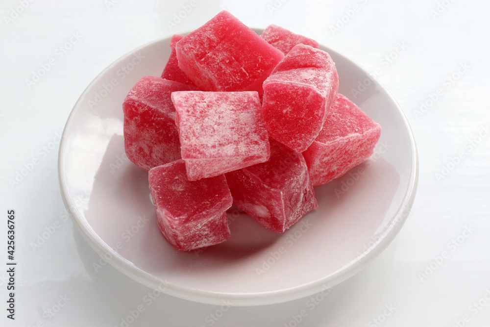 Red Turkish delights with sugar powder on plate on white table background. Oriental dessert sweet candy rahat locum. Top view, copy space Red Turkish delights with sugar powder on plate on white table background. Oriental dessert sweet candy rahat locum. Top view, copy space
