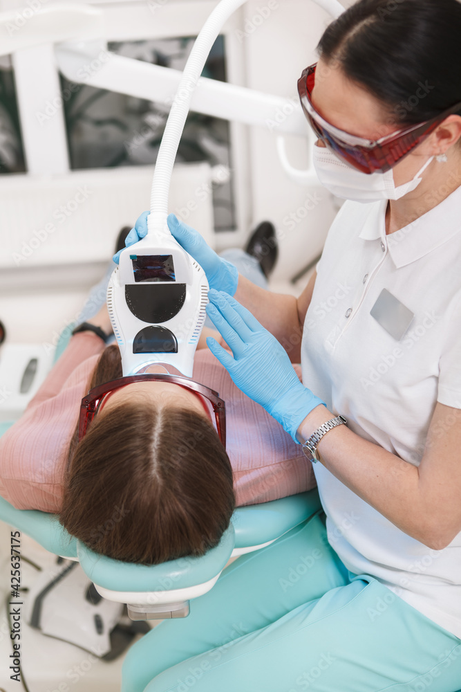 Vertical shot of a female dentist using modern teeth whitening equipment, working with patient Vertical shot of a female dentist using modern teeth whitening equipment, working with patient