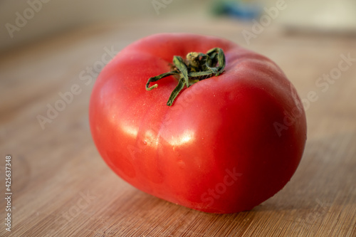 Red bright tomato on the wood background. Red tomato on a wooden background. One red tomato on a wooden background. One red tomato on a wooden countertop