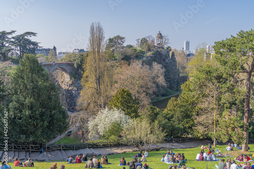 Paris, France - 04 04 2021: Park des Buttes Chaumont. People sit on the lawns of the park during the third lockdown