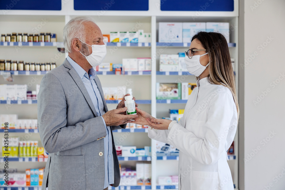 Prescriptions and drugs for therapy. An older man with gray hair in an elegant suit talks to a woman pharmacist. Talk about medical therapy, a protective mask against the corona virus. Drug handover