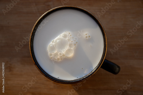 Glass of milk standing on old wooden table. Black glass with white milk. Black glass with white milk on the table