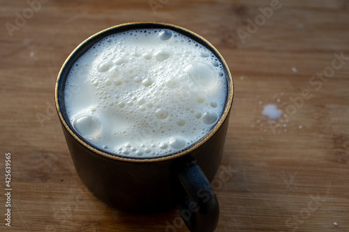 Glass of milk standing on old wooden table. Black glass with white milk. Black glass with white milk on the table