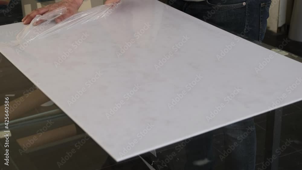 Man removing protective gelatin from the surface of white plastic material Man removing protective gelatin from the surface of white plastic material