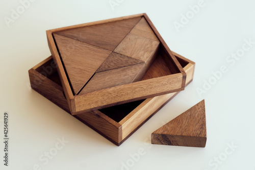 Close up kid's hand holding a piece of an wooden tangram puzzle on white table. Thinking. Mental developing. Playing, fun