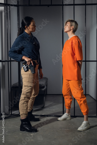 Asian warden and a female prisoner in a high-security prison stand in front of an open cell.