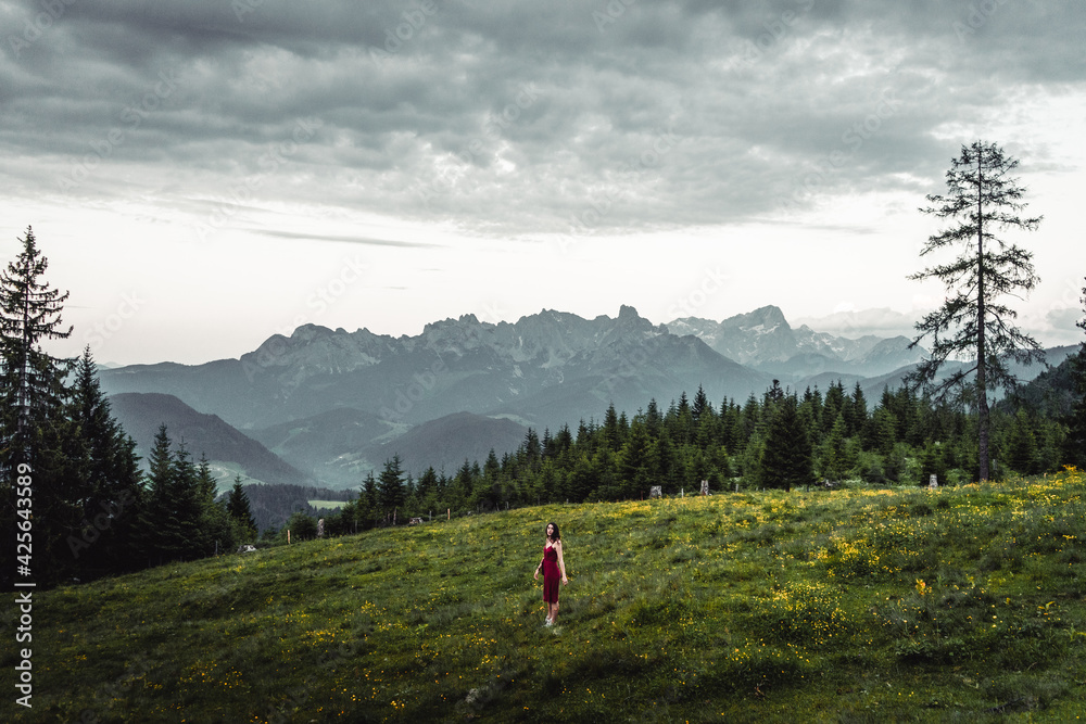 Naklejka premium Back view of slim young woman walking on grassy valley on background of green mountains on cloudy evening