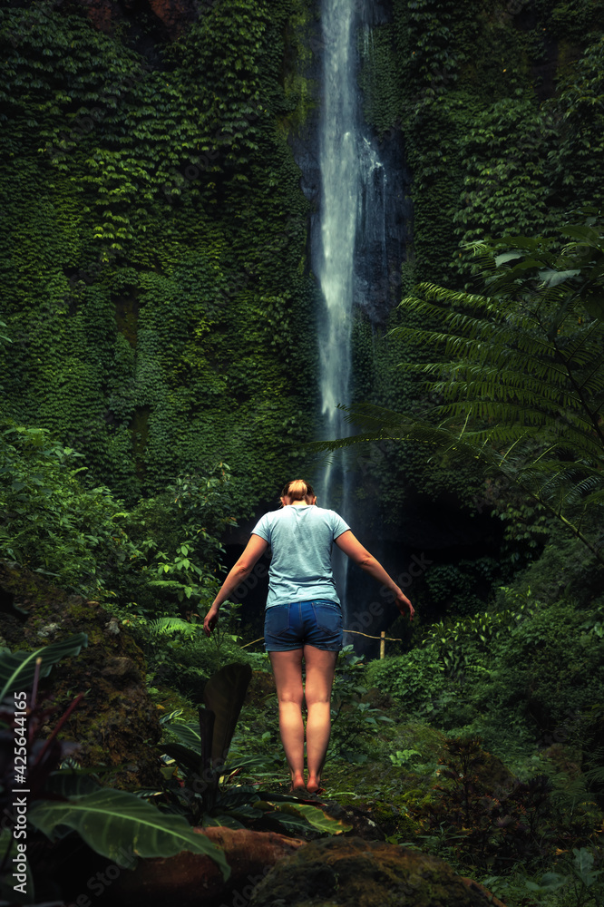 Woman traveler standing alone in rainforest and meditating nearby waterfall filled with nature energy as travel lifestyle and nature cognition