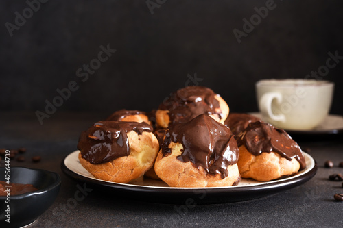Profiteroles with vanilla cream and chocolate sauce with a cup of coffee on the kitchen table. photo