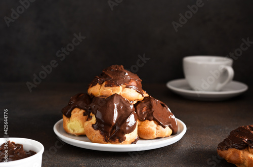фотографія Profiteroles with vanilla cream and chocolate sauce with a cup of coffee on the kitchen table