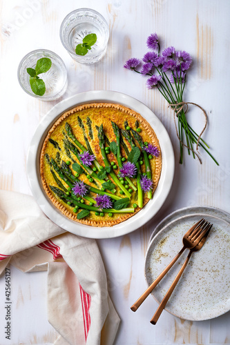 Green asparagus, sweet peas Tart with edible chives flowers or blossoms. Seasonal spring dinner table, overhead view.