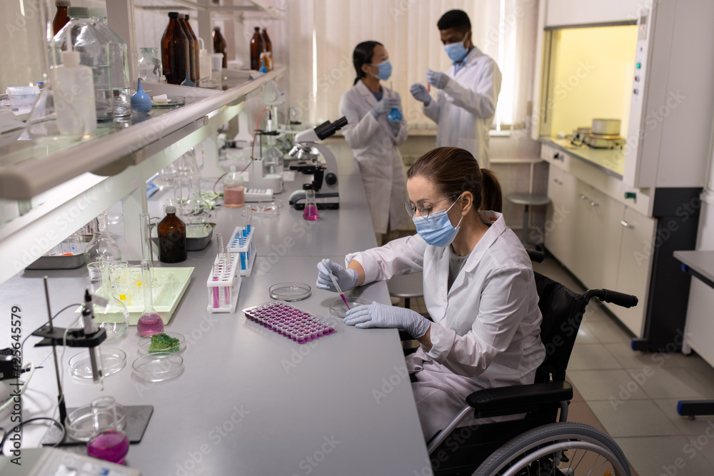 Chemist in mask examining liquid in test tubes while working with her colleagues in the laboratory Chemist in mask examining liquid in test tubes while working with her colleagues in the laboratory