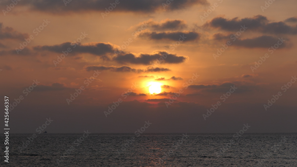 Sunset in the maldives with sun partly covered by clouds