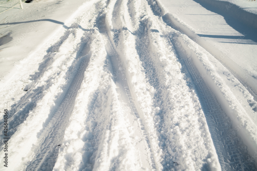 Obraz premium A lot of snow on the street on the road. Sunny day in cold weather. Winter day outside the city. Large snowdrifts in the cold season.